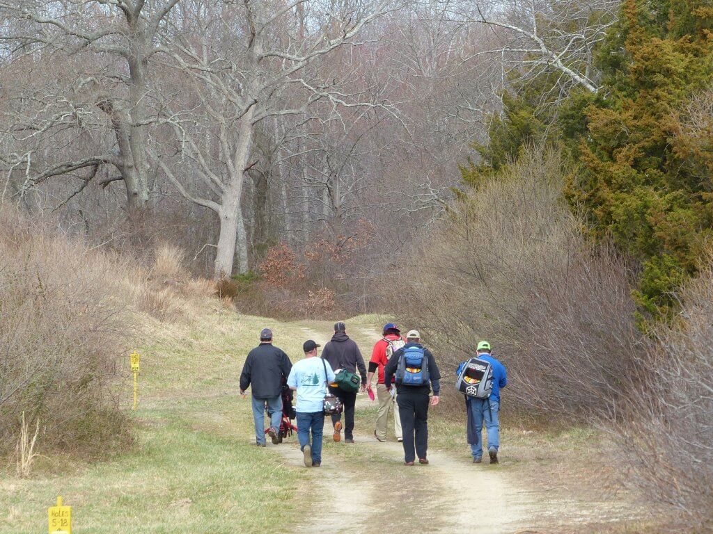 Group of disc golf players heads to tee in wooded area of Wisting Recreation Area March 12.