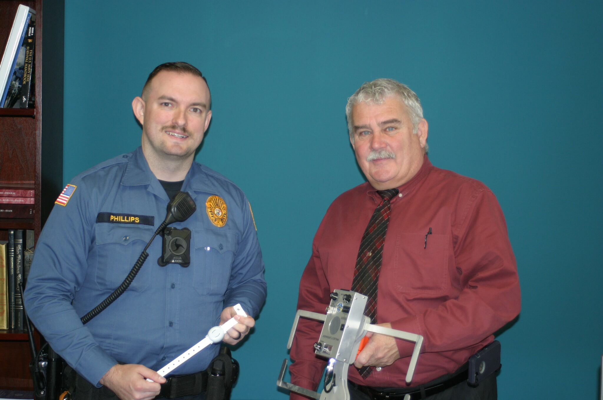 Cape May County Sheriff's Officer Dustin Phillips (left) is the coordinator for Project Lifesaver. He is holding the band transmitter that clients wear. The vinyl band can be worn on the wrist or ankle. Sheriff Robert Nolan holds one of seven receivers officers use to locate missing clients.