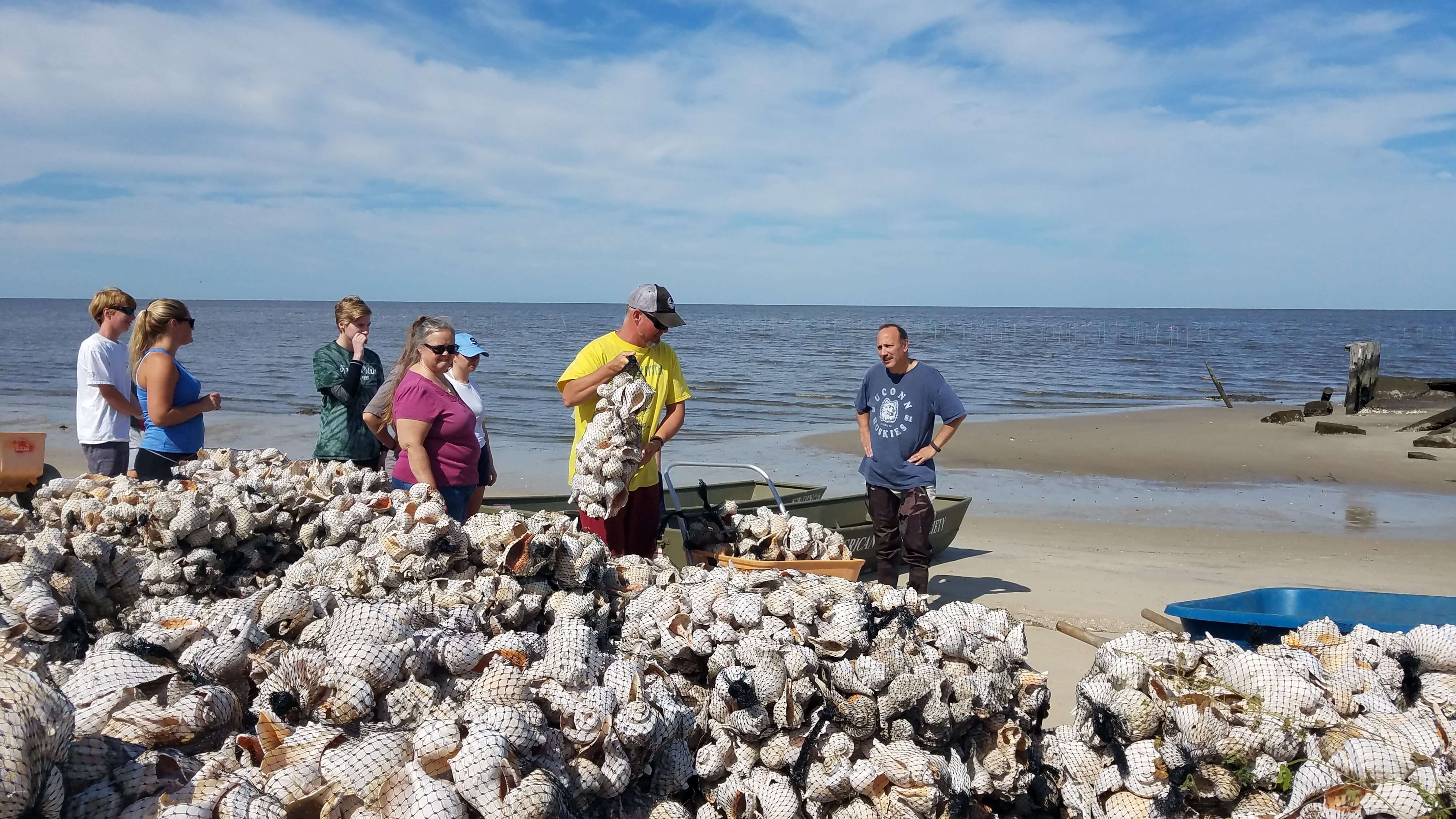 Capt. Alek Modjeski (wearing hat) shows volunteers and staff what needs to be done to build three reefs out of bags of recycled whelk shells.
