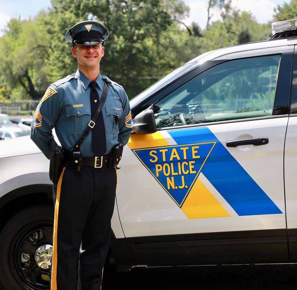 Detective Sgt. First Class George Wren posing with a state police vehicle. 
