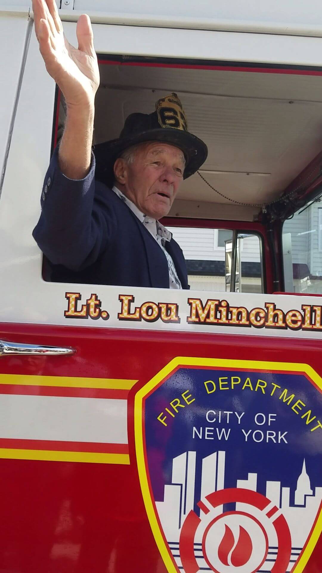 Retired FDNY Lt. Lou Minchelli waves from cab of the fire truck he received on his 90th birthday.