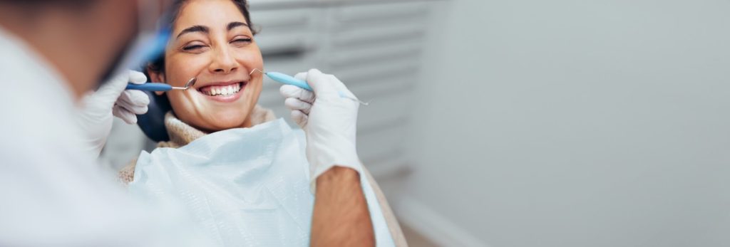 Happy woman getting dental checkup at dentistry. Dentist using dental equipment for examination of teeth of a female patient.