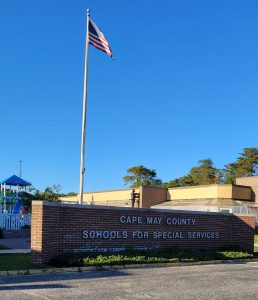 The sign of the school sits in the afternoon sunshine with the new playground in the background. The Special Services School District