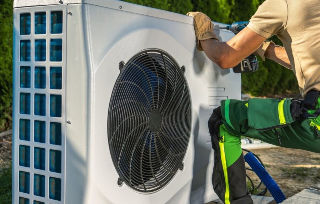 An HVAC worker installs an electric heat pump in this stock photo.